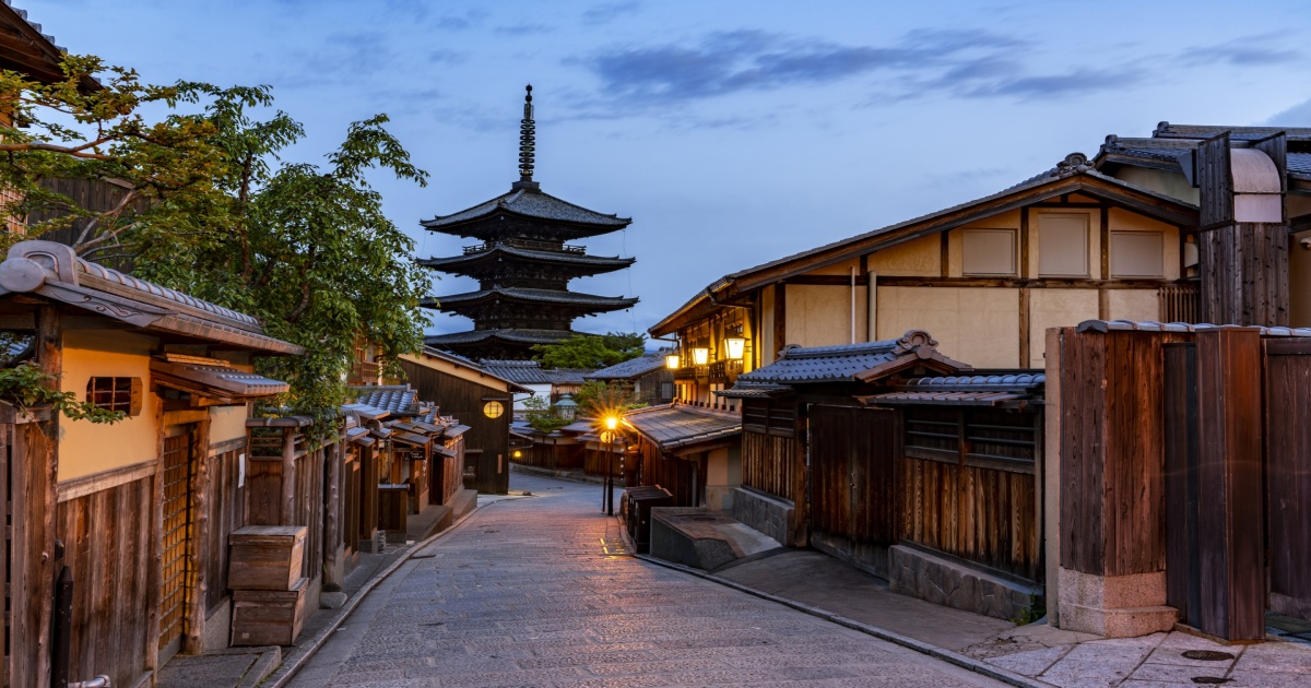 京都・東山の町並みを背景に立つ八坂の塔（法観寺）の五重塔。夕暮れに映える古都の風景。