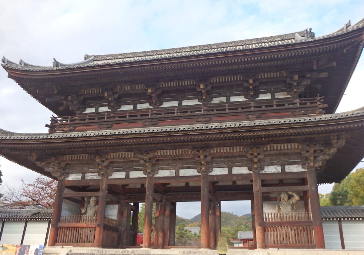 仁和寺の巨大な二王門。門の左右に力強い仁王像が鎮座し、参拝者を圧倒する様子。